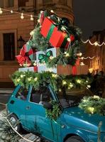 viejo coche vintage de santa con cajas de regalo en la parte superior. ramas de primer plano de árboles coníferos decorados con guirnaldas de luz brillante. contenido festivo perfecto para el fondo de las historias, banner vertical. foto