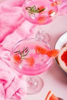 Homemade pink cocktail with ice and rosemary in glasses on the table. Vertical view photo