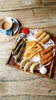 plato de aperitivos compuesto por patatas fritas, otak otak, patas de dragón, dimsum, rollitos de primavera con salsa de tomate y mozzarella foto