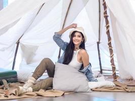 Portrait beautiful young girl woman Asian pretty smile one person alone sitting on chair camping with teble flower in vase lantern red travel trip in front tent freedom relax happy enjoy in vacation photo