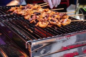 Cierre la brocheta de carne de calamar cruda en hoja de plátano en el mercado de productos frescos de Tailandia con salsa de marisco picante. Comida callejera de Tailandia foto