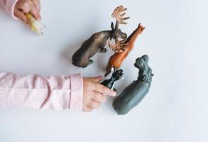 Little girl toddler playing with animal toys on table in children's room at home, view fron top photo