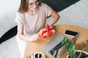 mujer joven con anteojos haciendo compras en línea en una laptop en casa foto