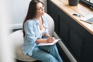 Young woman in bue shirt with notes in hands sitting on chair in room photo