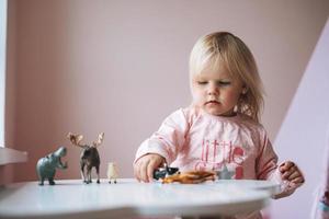 Little girl toddler in pink playing with animal toys on table in children's room at home photo