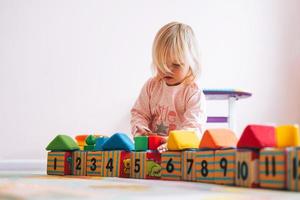 Little girl toddler in pink playing with blocks with numbers in children's room at home photo