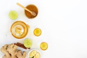 vista superior de una taza de té con raíz de jengibre, lima, canela y tetera sobre fondo blanco. concepto de bebida saludable foto
