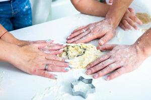 familia cocinando pasteles caseros. manos de mamás y niños sosteniendo cortadores de galletas. cocina familiar endecha plana. dulce hogar. concepto de felicidad. foto