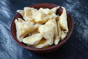 Traditional russian pelmeni or ravioli, dumplings with meat on wood black background. Russian food and russian kitchen concept. photo