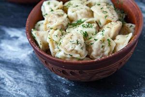 Traditional russian pelmeni or ravioli, dumplings with meat on wood black background. Russian food and russian kitchen concept. photo