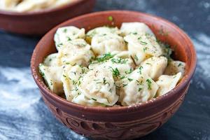 Traditional russian pelmeni or ravioli, dumplings with meat on wood black background. Russian food and russian kitchen concept. photo