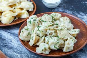 Traditional russian pelmeni or ravioli, dumplings with meat on wood black background. Russian food and russian kitchen concept. photo