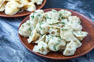 Traditional russian pelmeni or ravioli, dumplings with meat on wood black background. Russian food and russian kitchen concept. photo