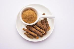 Ayurvedic Mulethi or Liquorice root stick or jeshthamadh powder served in a bowl over moody background photo