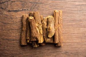 Ayurvedic Mulethi or Liquorice root stick or jeshthamadh powder served in a bowl over moody background photo