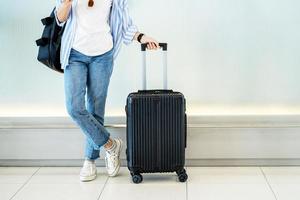 mujer asiática adolescente usando un teléfono inteligente en la terminal del aeropuerto de pie con maleta de equipaje y mochila para viajar en vacaciones de verano foto