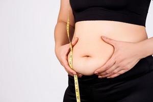 mujer gorda sosteniendo grasa abdominal excesiva con cinta métrica sobre fondo blanco. endurecimiento de los músculos abdominales. concepto de obesidad. foto