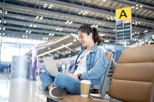 Attractive female tourist working with laptop in airport terminal. Freelancer student travels to business meeting. photo