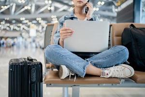 Travel vacation concept, asian female woman uses a smartphone and is working on a laptop, she sit wating for flight schedule at terminal airport. photo