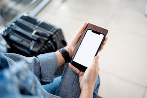 Traveler showing empty space on phone in hand with suitcase in airport terminal photo