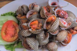 Steamed cockles boiled cockles are placed on a white plate. Garnished with sliced tomatoes. photo