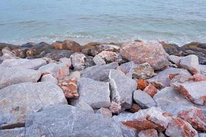 pile of rocks by the sea with the sea waves crashing to shore. photo