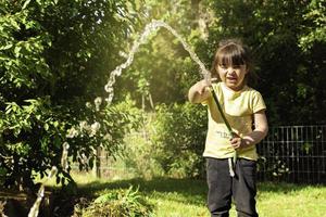 niña divirtiéndose con el riego de árboles y plantas en el jardín doméstico foto