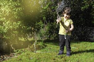 linda niña de 3 años regando y jugando con una manguera de jardín. enfoque selectivo foto