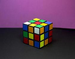 Unsolved rubik cube game for training the brain. Fun educational logic training photo isolated on purple and black surface background wallpaper.