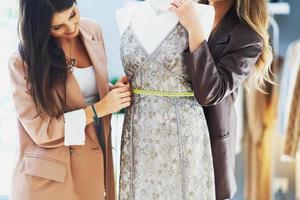 Two women tailors trying dress on mannequin photo