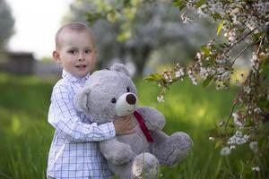 un niño feliz en un jardín floreciente sostiene un oso de juguete. foto
