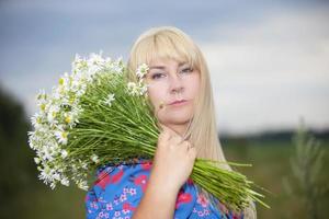 A beautiful plus size girl with white hair in a summer dress poses on the street with daisies. Chubby girl in a meadow with daisies close-up. photo