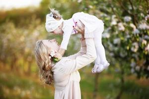 mamá con una pequeña hija en un jardín floreciente. maternidad feliz feliz retrato de madre y pequeña hija al aire libre. concepto del día de la madre foto