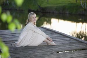 hermosa joven rubia en un puente de madera cerca del río posando, mirando a la cámara. foto