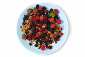 On a white background a plate with summer berries. Fruit salad with raspberries, gooseberries, currants, mulberries. Flat lay, top view photo