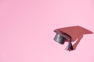 gorra negra graduada en miniatura sobre fondo rosa. concepto de educación foto