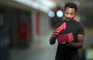 hombre abriendo caja mirando dentro de regalo de navidad sorpresa expresión emocionada con centro comercial luz bokeh foto