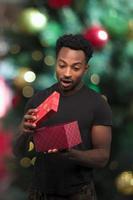 hombre abriendo caja mirando dentro de regalo de navidad sorpresa expresión emocionada con luz bokeh foto