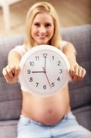 Happy pregnant woman resting on sofa and holding clock photo