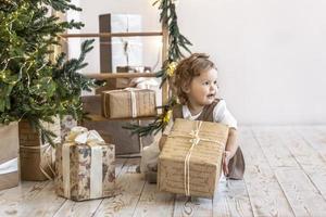 A little girl at the Christmas tree with boxes of gifts. Unpacking gifts, emotions,childhood. photo