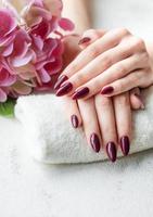 manos de una mujer joven con manicura roja oscura en las uñas foto