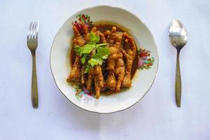 Spicy chicken feet with celery, chili, onion, garlic served with a white plate isolated from a black background. photo