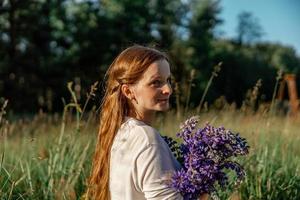 Close up portrait of young beautiful redhead woman with freckles, wearing white dress, posing in the nature. Girl with red hair holding flowers. Natural beauty. Diversity, individual uniqueness. photo