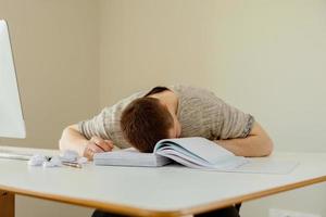 hombre caucásico deprimido con dolor de cabeza sentado en su escritorio en la oficina. El joven empleado estresado tiene problemas en el trabajo. el empresario tiene agotamiento. salud mental. abrumado por el trabajo. plazo, estrés. foto