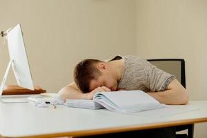 hombre caucásico deprimido con dolor de cabeza sentado en su escritorio en la oficina. El joven empleado estresado tiene problemas en el trabajo. el empresario tiene agotamiento. salud mental. abrumado por el trabajo. plazo, estrés. foto