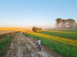 Little boy riding bike in countryside. Riding person at sunset in nature. Child spending his free time active. Freedom, beautiful landscape. Happy childhood. photo