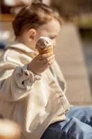 Little adorable boy sitting outdoors and eating ice cream. Lake, water and sunny weather. Child and sweets, sugar. Kid enjoy a delicious dessert. Preschool child with casual clothing. Positive emotion photo