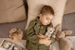 Little and cute caucasian boy fell asleep after reading a book on the bed at home. Interior and clothes in natural earth colors. Cozy environment. Child resting, sleeping. photo