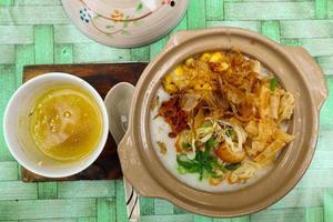 porridge served on hot claypot topped with chicken, sweet corn, skipjack tuna, tofu, green onions, crackers, dumplings and broth photo