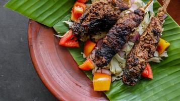 sate buntel or satay buntel is satay made from minced mutton wrapped in mutton fat and then grilled. seasoning with tomatoes, shallots, pepper, cabbage photo